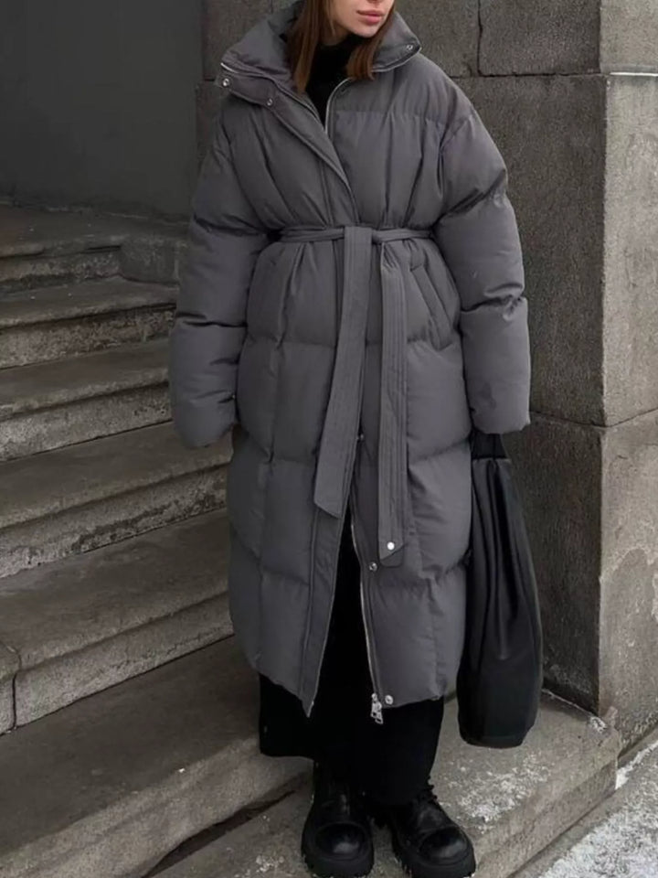 Modelo posando con abrigo largo acolchado y cinturón, destacando la elegancia de la prenda invernal.