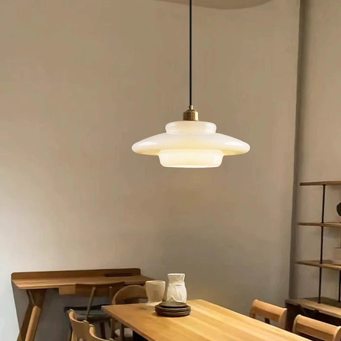 Lámpara colgante Mid-Century encendida, luz cálida a través del cristal marfil, latón brillante.