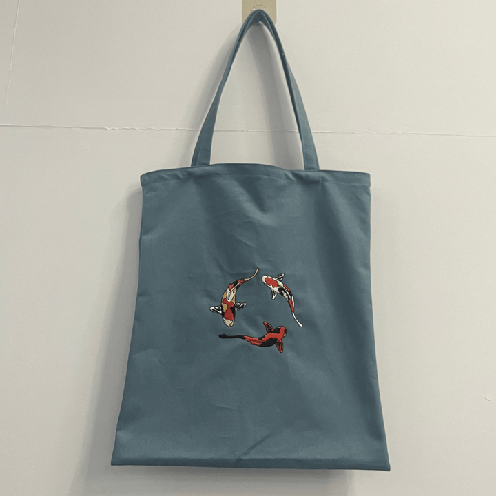 Bolso tote de lona verde azulado para mujer con elegante bordado de pez koi. Ideal para uso diario o casual.