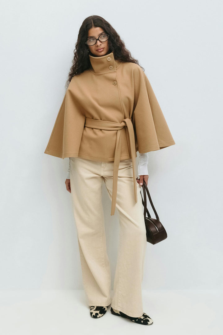 Abrigo capa de mujer con cuello alto y cinturón, textura suave. Moda invernal elegante.