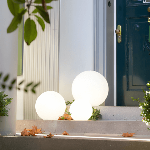 Lámpara solar esférica LED iluminando camino de jardín al anochecer. Luz exterior automática.