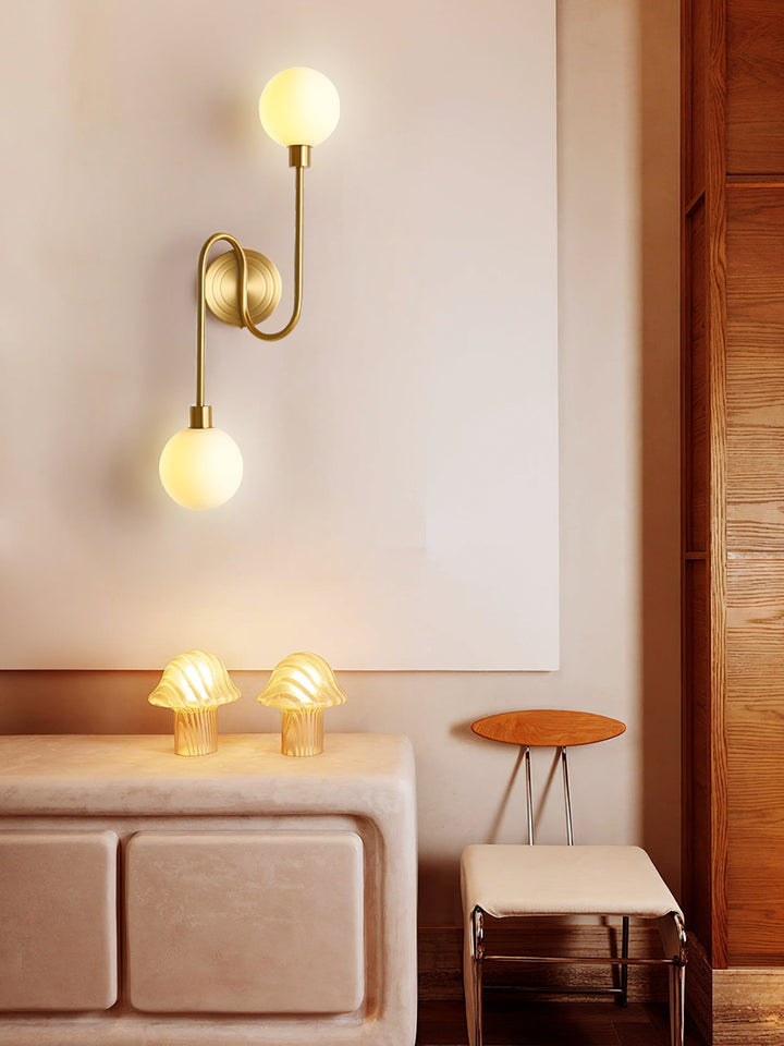 Aplique moderno de latón dorado y dos globos de cristal blanco. Crea un ambiente cálido.