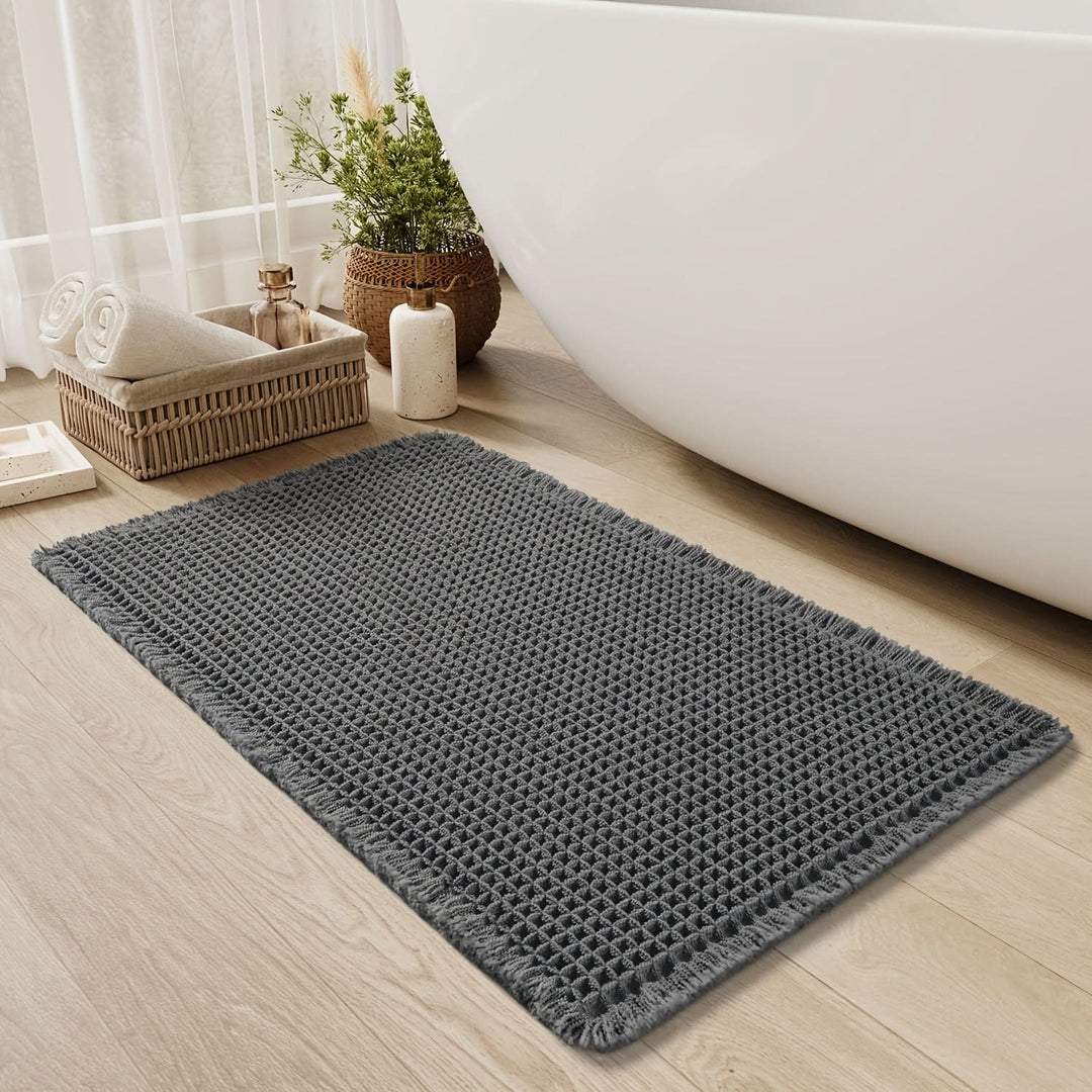 Detalle de alfombrilla de baño tipo waffle con flecos. Textura suave, absorbente y de secado rápido.
