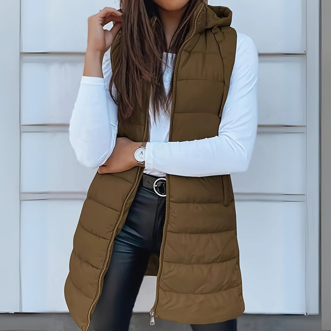 Mujer vistiendo chaleco largo acolchado gris con capucha. Prenda versátil y cálida para moda de invierno.