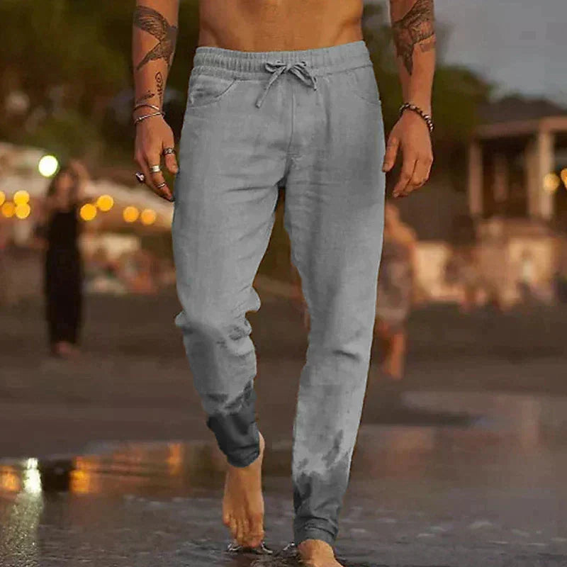 Hombre en la playa con pantalones de lino relajados, cómodos y transpirables para vacaciones de verano.