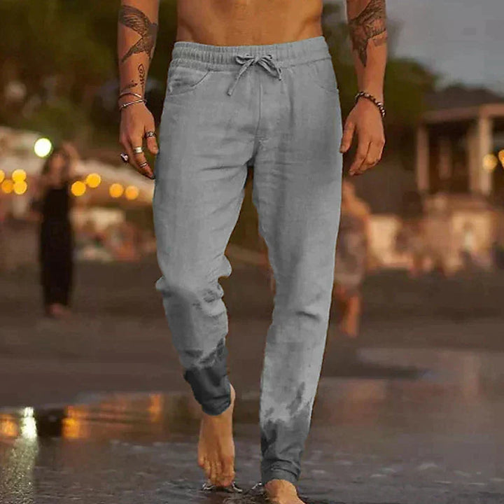 Hombre en la playa con pantalones de lino relajados, cómodos y transpirables para vacaciones de verano.