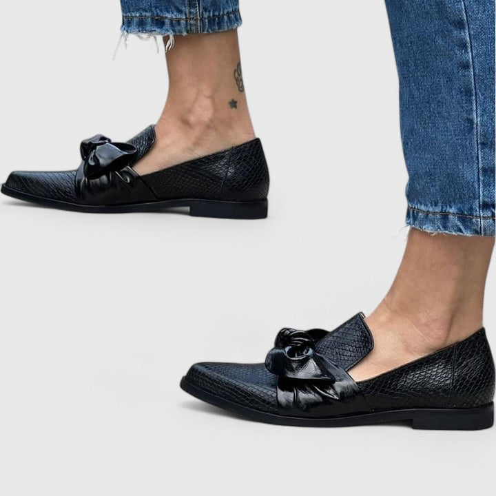 Mujer luciendo mocasines negros elegantes con lazo. Zapatos cómodos sin cordones para un estilo chic y casual.