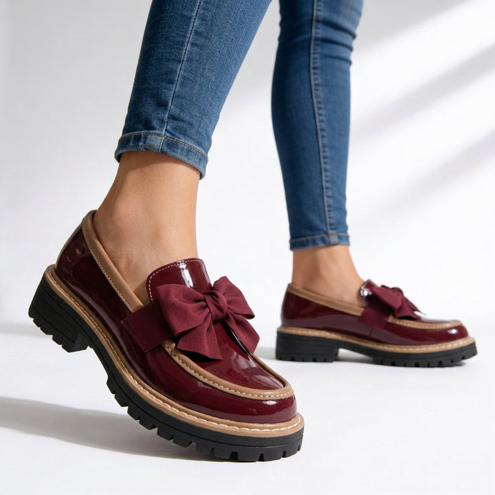 Detalle de mocasín de mujer en charol. Presenta un lazo clásico y suela gruesa, combinando confort y un toque moderno.