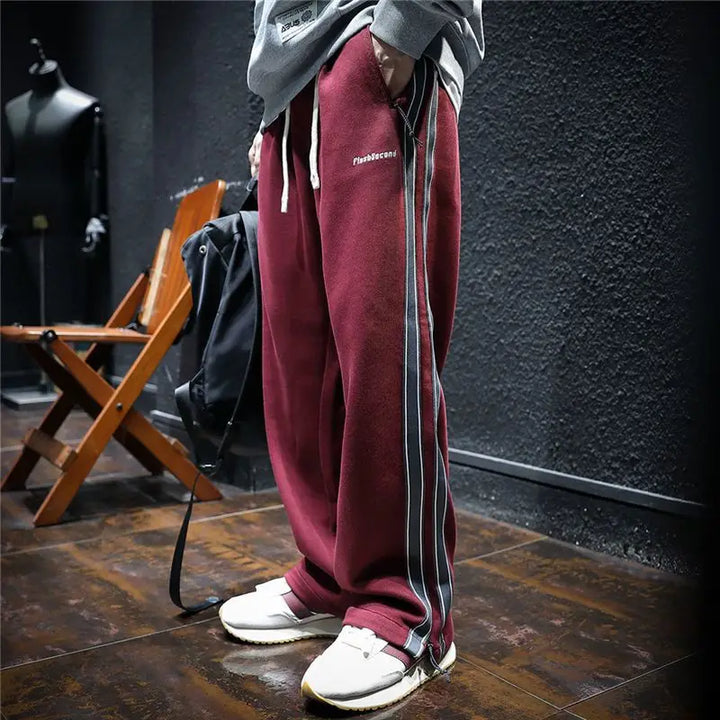 Pantalones anchos negros de hombre con rayas rojas laterales. Ajustables, cremallera, ideal estilo urbano.