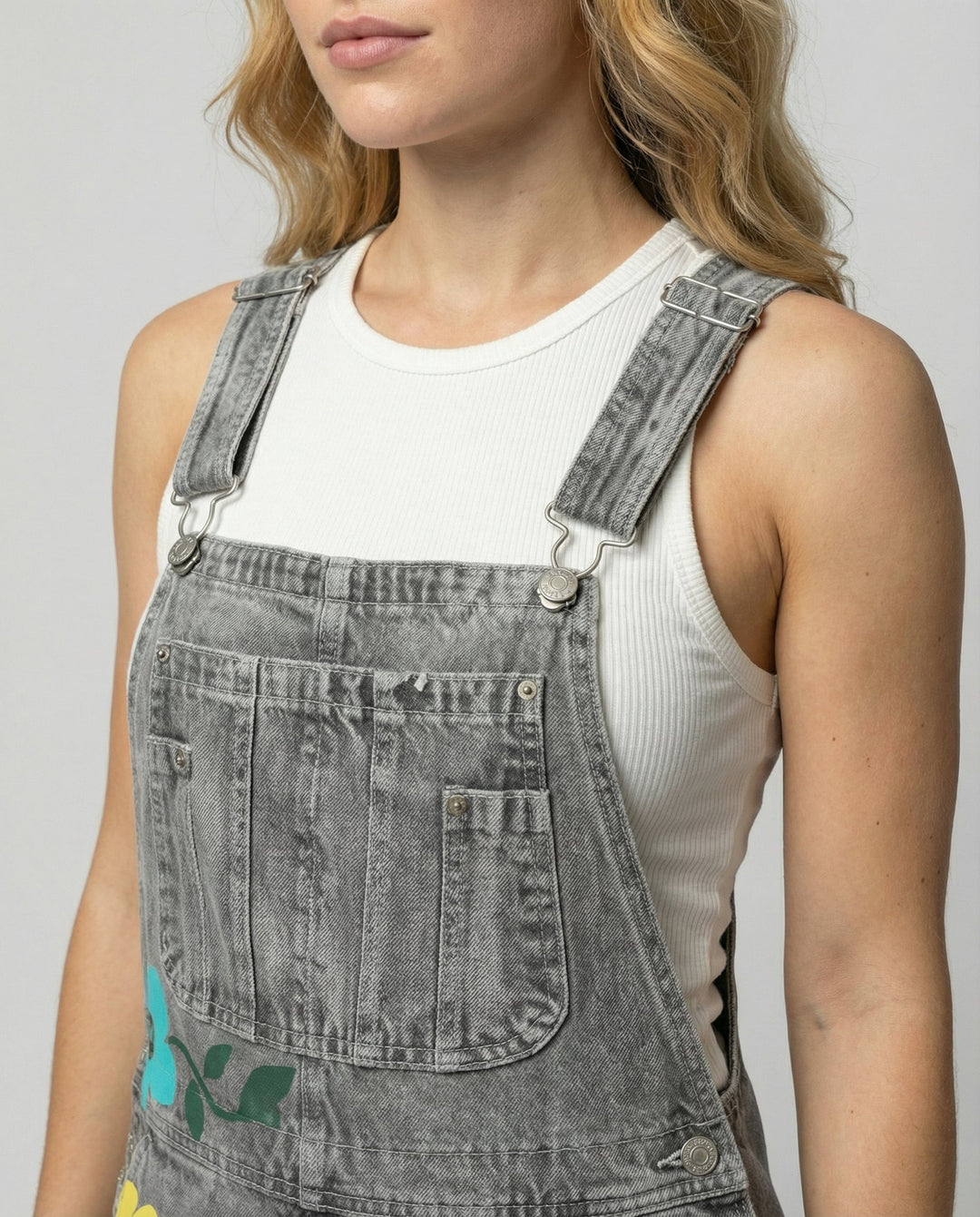 Detalle de peto de mezclilla para mujer con patrón floral vibrante y tirantes ajustables, look fresco.