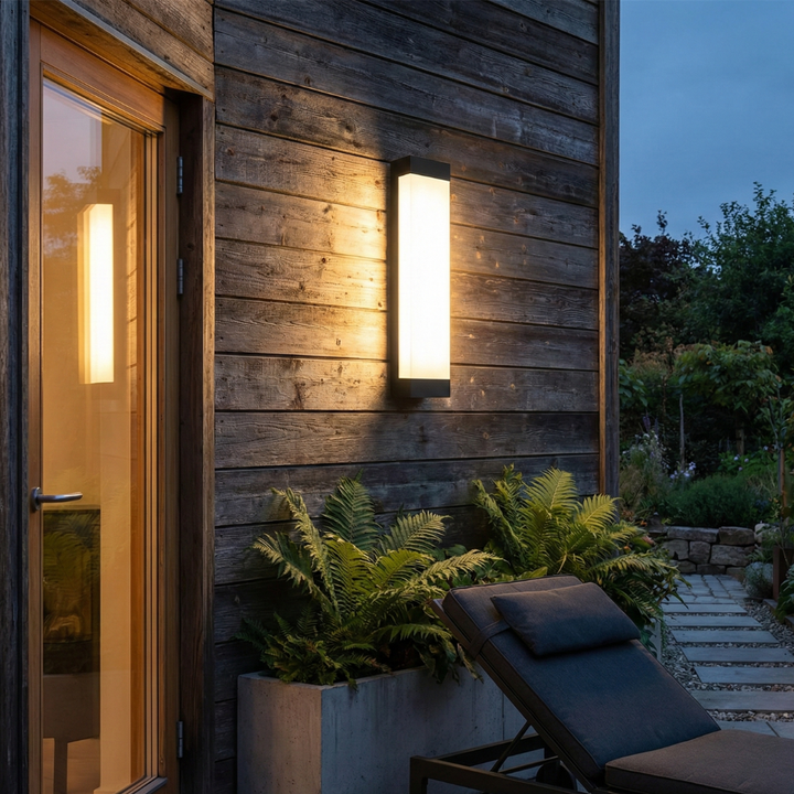 Luz de pared exterior LED iluminando un jardín por la noche. Iluminación cálida y moderna para seguridad.