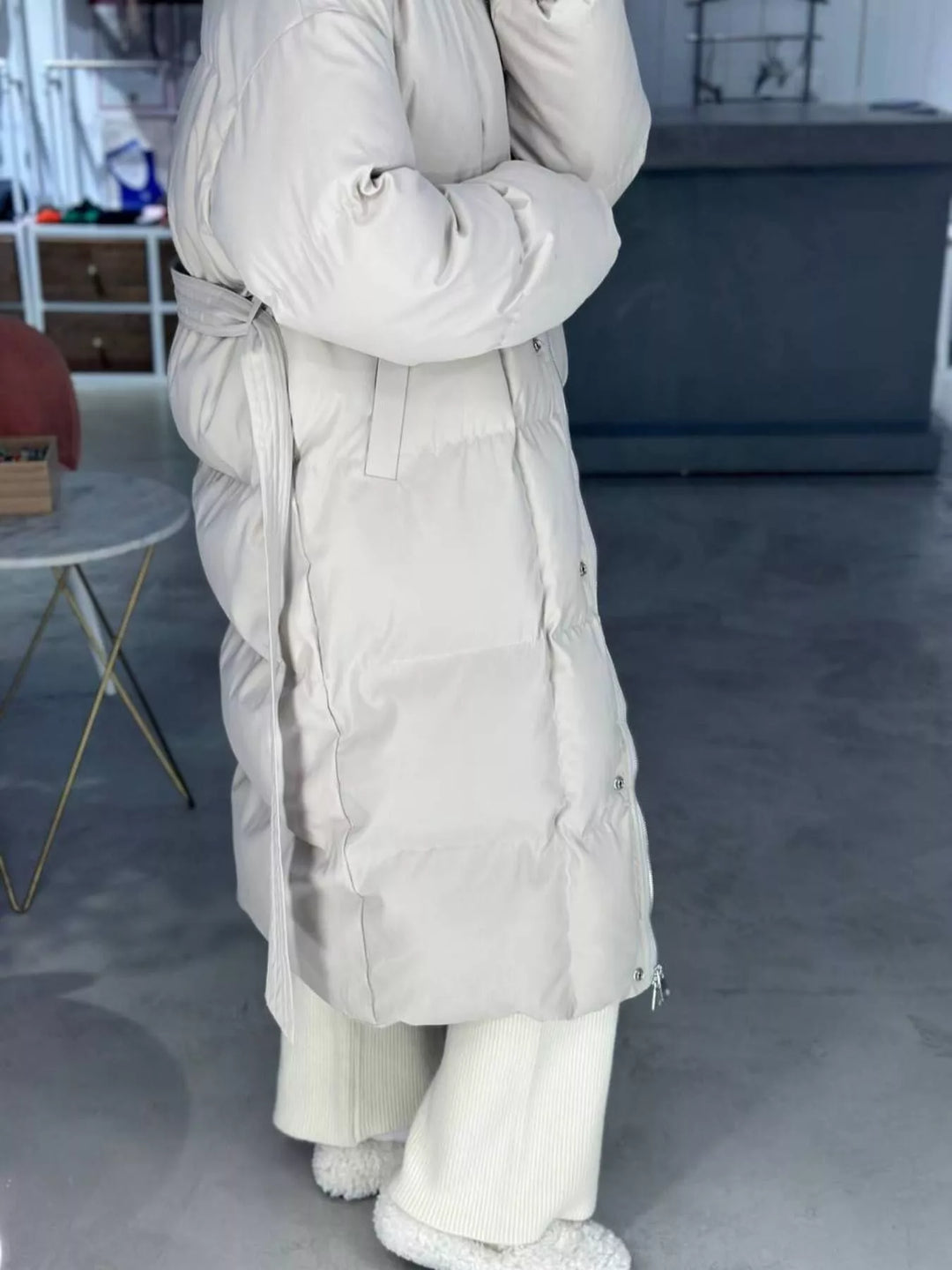 Mujer usando un abrigo acolchado largo con cinturón, destacando su silueta, moda casual invernal.