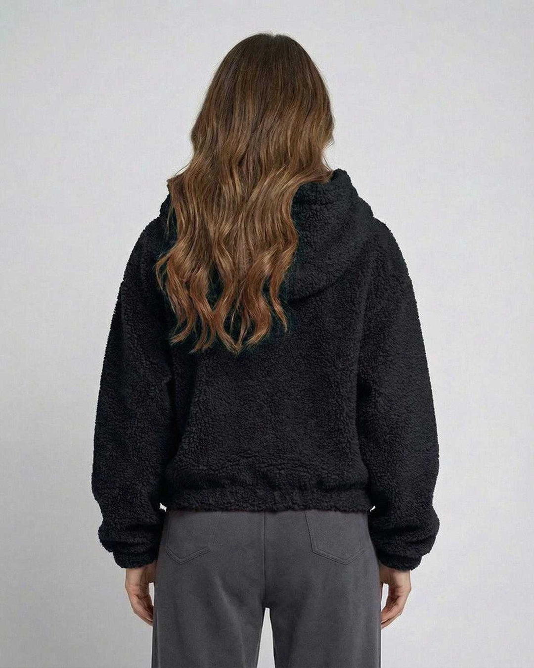Mujer con chaqueta corta negra de capucha y cremallera, estilo urbano moderno y cómodo para el día a día.