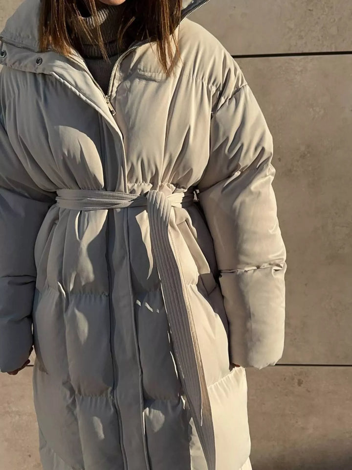 Elegante abrigo largo acolchado para mujer con cinturón, vista frontal, moda invernal sofisticada.
