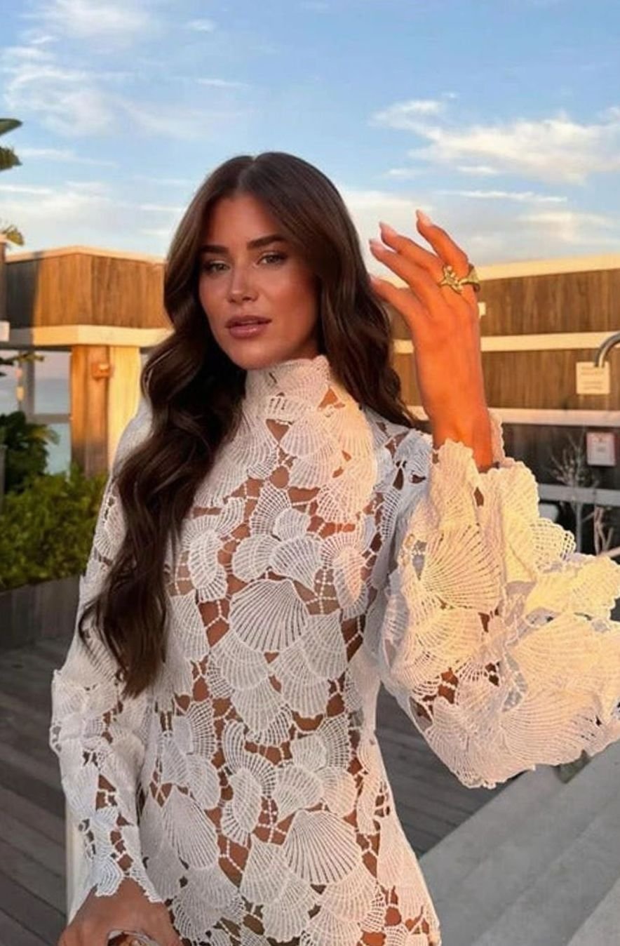 Elegante vestido de cóctel para mujer con encaje floral blanco, cuello alto y manga larga, silueta entallada.