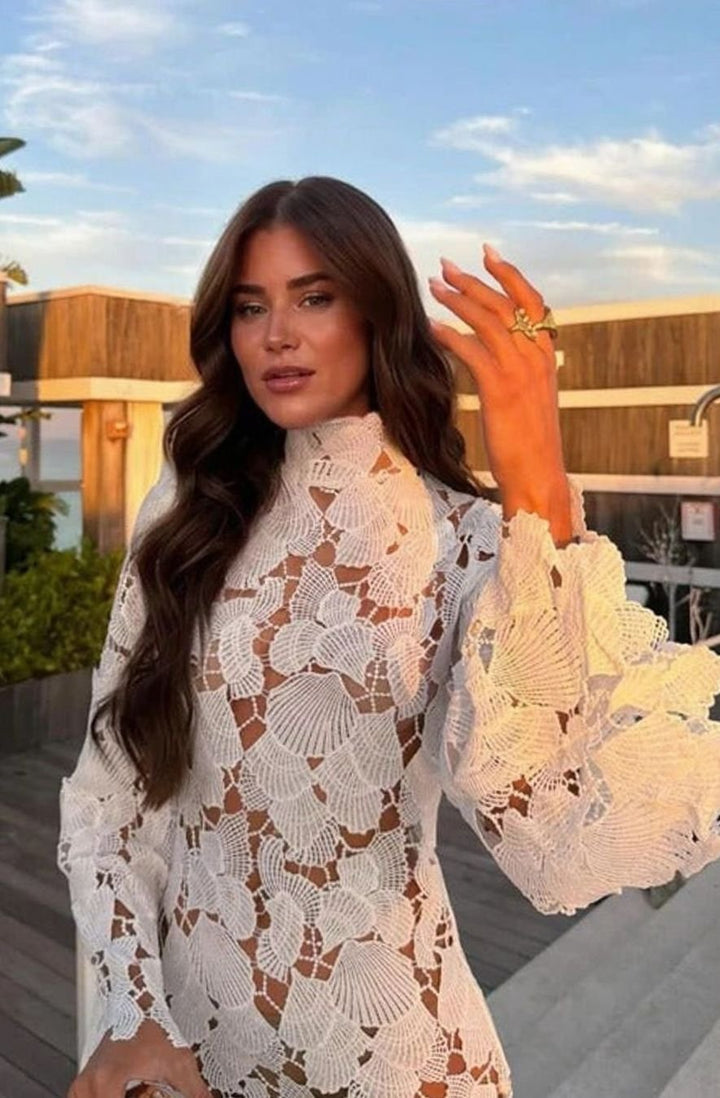 Elegante vestido de cóctel para mujer con encaje floral blanco, cuello alto y manga larga, silueta entallada.