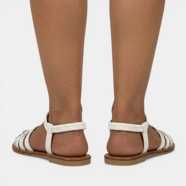 Mujer llevando sandalias planas de tirantes cruzados. Comodidad diaria y estilo veraniego, perfectas para pasear.