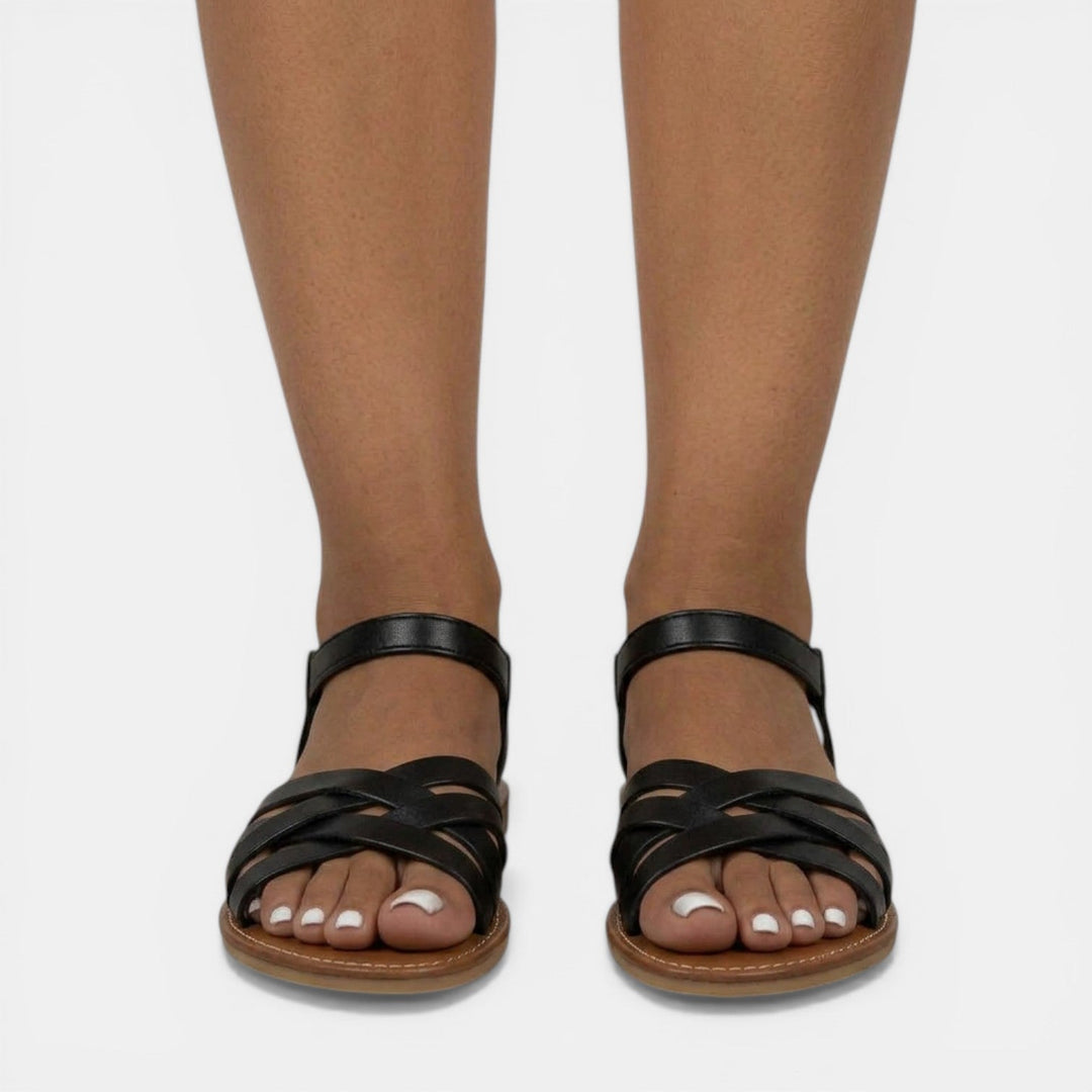 Primer plano de sandalias planas de mujer, tirantes cruzados. Material suave y flexible para máxima comodidad veraniega.