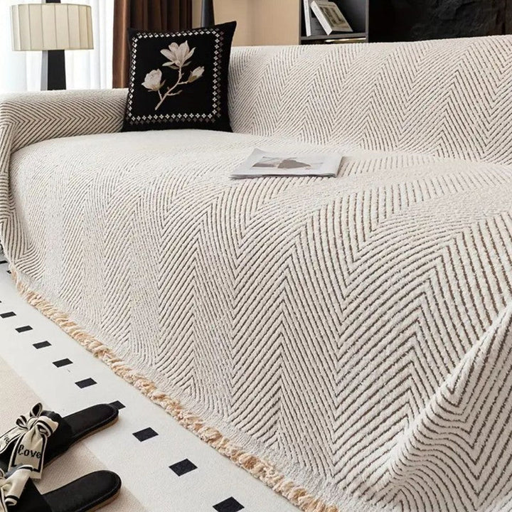 Protector de sofá con diseño drapeado y flecos. Tejido espiga, ideal para textil hogar y decoración.