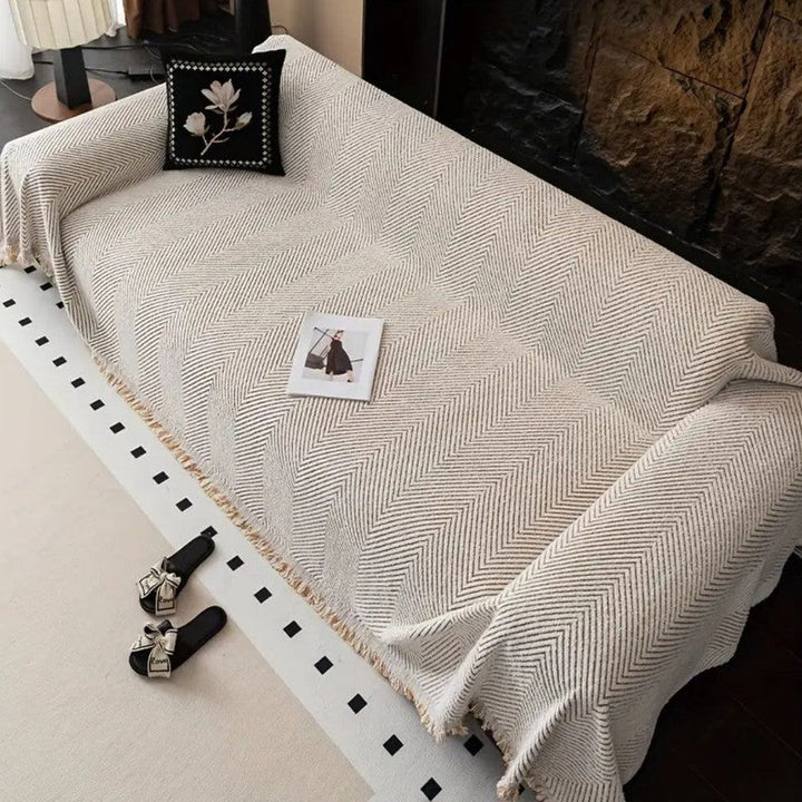 Funda para sofá con elegante textura espiga y flecos. Aporta calidez y estilo acogedor a tu sala de estar.