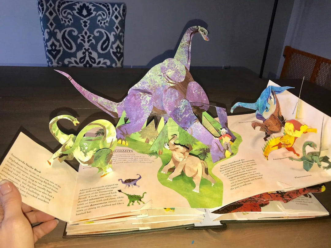Libro pop-up 3D de dinosaurios abierto, revelando escenas prehistóricas. Fomenta el aprendizaje y la diversión.