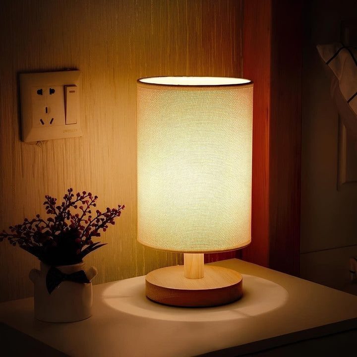 Lámpara de mesa LED cilíndrica con control táctil, base de madera. Aporta luz moderna y funcional.