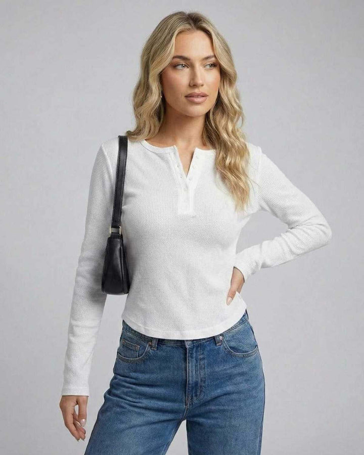 Modelo luciendo top blanco ajustado de manga larga, creando un atuendo elegante y versátil.