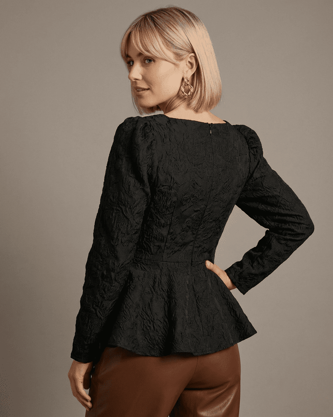 Mujer vistiendo top corsé negro estructurado con mangas abullonadas. Blusa elegante y moderna.
