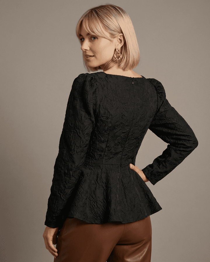 Mujer vistiendo top corsé negro estructurado con mangas abullonadas. Blusa elegante y moderna.