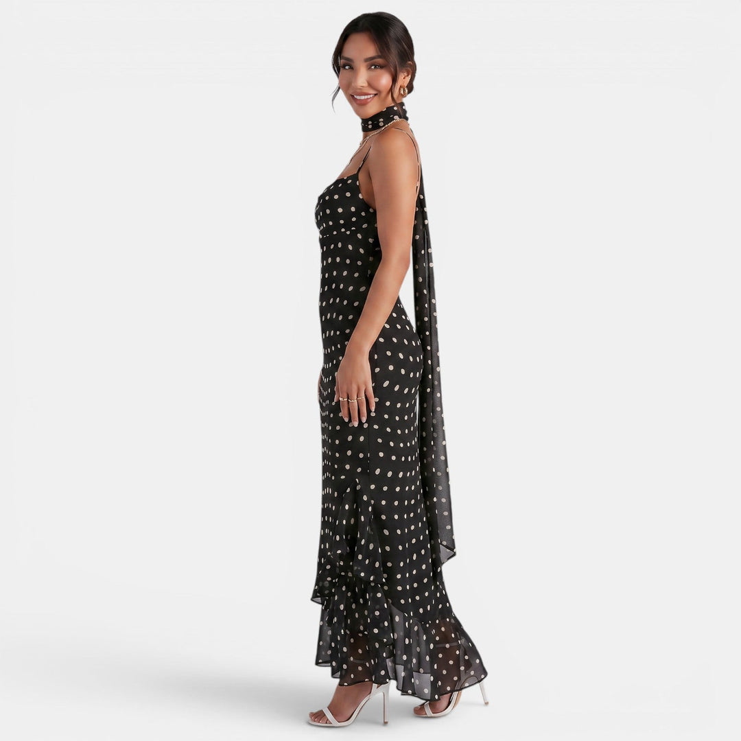 Mujer luciendo elegante vestido maxi halter negro con lunares, diseño atemporal y fluido ideal para eventos de verano.