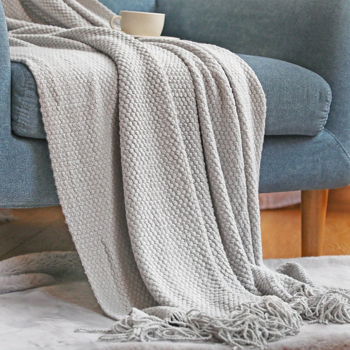 Manta tejida gris sobre sofá con cojines decorativos, crea ambiente escandinavo confortable para el hogar.