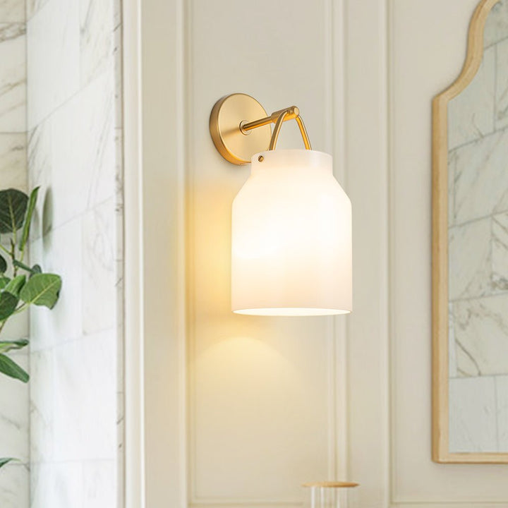 Aplique de pared nórdico con vidrio cilíndrico y base de latón pulido. Ideal para luz ambiental.