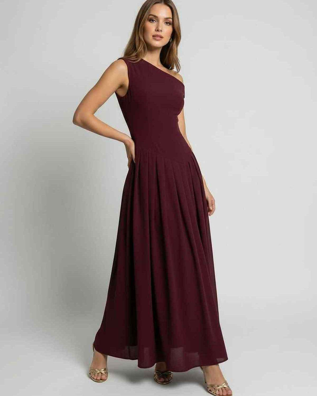 Mujer luciendo vestido maxi burdeos formal. Diseño fluido sin mangas, escote asimétrico para invitada de boda.