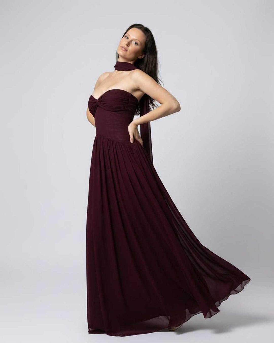 Mujer luce vestido maxi burdeos sin tirantes, estilo formal y fluyente, perfecto para bodas y galas.
